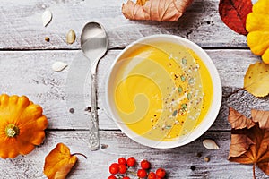 Autumn pumpkin soup decorated seeds and thyme in white bowl on rustic wooden table top view. Cozy lifestyle shot for halloween.