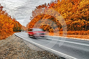 autumn pursuit chase. asphalt road and fast fury red car in motion on cloudy day. Travel auto trip autumn rain road in forest