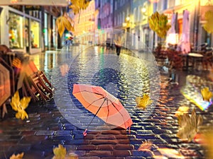 Autumn rain in city blurred light lamp pink umbrella on asphalt pavement yellow leaves fall on road night city street Tallinn Old