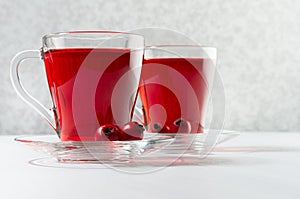 Autumn red herbal tea in two transparent cups with ripe hawthorn berries in sunlight on white wood table, closeup.