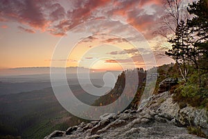 Autumn rocky landscape within sunset. Colorful sky above deep misty valley full of evening humidity. Sun on horizon.