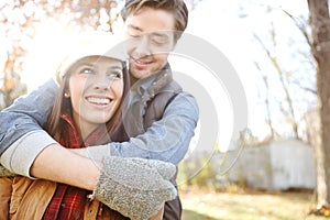 Autumn romance. A handsome young man embracing his girlfriend while they spend time out in nature.