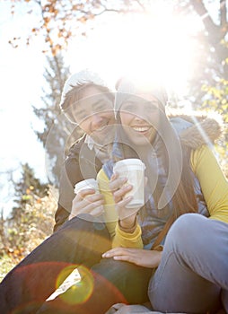 Autumn Romance. A romantic young couple sitting close together while enjoying some coffee in the outdoors.