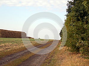 Autumn rural road and haystack under clear sky