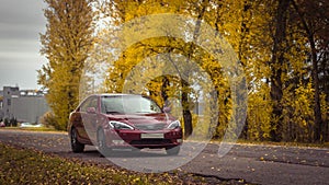 Autumn scene with Cherry red 4 door family d-class sedan Toyota Camry