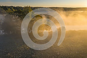 Autumn scene in morning sunlight on misty riverside. Bright warm sun light through fog and trees aerial view. Beautiful october