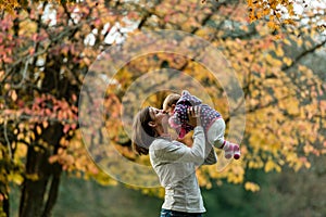 Autumn scene of mother kissing young baby girl outdoors