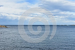 Autumn seascape background. Blue sea with rocks and foam, horizon, cloudy sky.