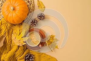 Autumn season concept with coffee cup, warm sweater, fall leaves and pumpkin on beige background. Top view, flat lay