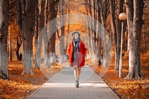 Autumn season. Elegant beautiful mature caucasian woman in a red coat and hat walks along the path of the autumn Park