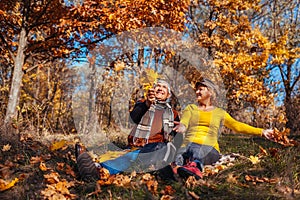 Autumn season fun. Senior couple throwing leaves sitting in park. Man and woman relaxing outdoors