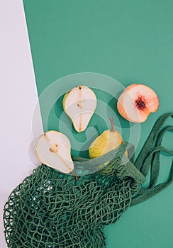 Autumn season minimalist scene. Organic pears, peach and mesh bag on green and white background. Zero waste, bio, eco, vegan