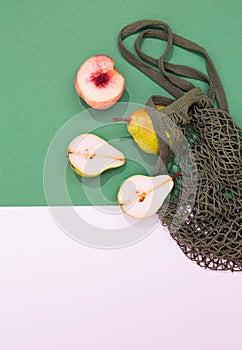 Autumn season minimalist scene. Organic pears, peach and mesh bag on green and white background. Zero waste, bio, eco, vegan