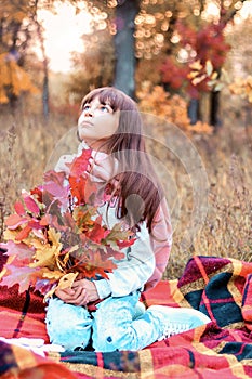 Autumn season nature cute teen girl portrait in warm pink scarf sitting on checkered blanket with bouquet in hands