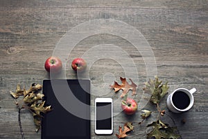 Autumn season still life with red apples, mobile devices, black coffee cup and fall leaves over rustic wooden background. Knolling