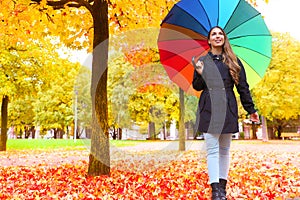 Autumn season. Young woman walking in city park under colorful rain umbrella