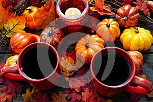 Autumn setting with small pumpkins and a red candle holder emitting light on two cups of morning coffee