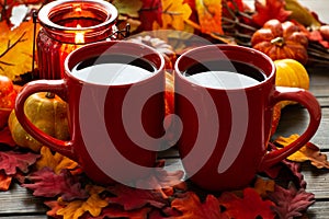 Autumn setting with small pumpkins and a red candle holder emitting light on two cups of morning coffee