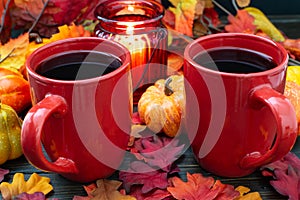 Autumn setting with small pumpkins and a red candle holder emitting light on two cups of morning coffee