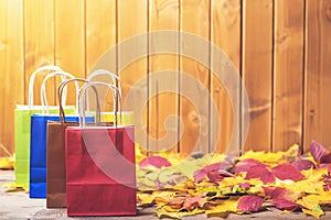 Autumn shopping. Color paper bags for shopping on fallen leaves over wooden background. Copy space. Autumn sales. A lot of colorfu