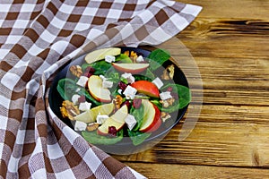 Autumn spinach salad with apple, feta cheese, walnut and dried cranberry on wooden table. Healthy vegetarian food