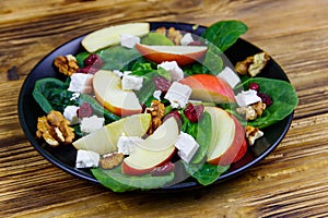 Autumn spinach salad with apple, feta cheese, walnut and dried cranberry on wooden table. Healthy vegetarian food