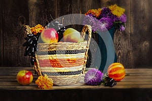 Autumn still life with apples and grapes in a basket. Purple asters and marigolds in a blue vase, pumpkin.