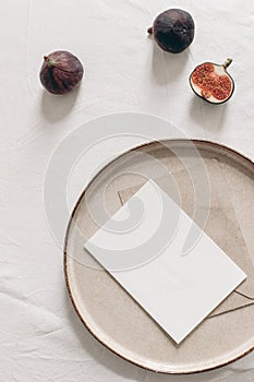 Autumn still life. Blank greeting card mockup, cut figs fruit and ceramic plate on white linen table cloth background