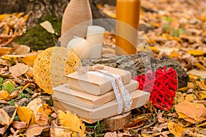 Autumn still life. Books in kraft paper covers, wicker red heart, ball of braided threads, candles, yellow leaves and tree bark.