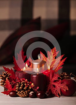 Autumn still life - candles, leaves and cones on the background of pillows