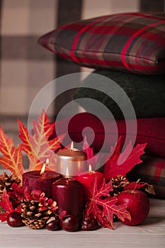 Autumn still life - candles, leaves and cones on the background of pillows