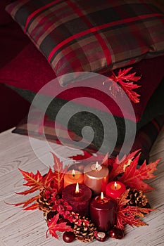 Autumn still life - candles, leaves and cones on the background of pillows