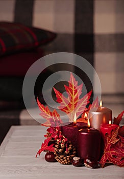 Autumn still life - candles, leaves and cones on the background of pillows