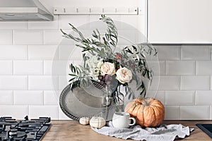 Autumn still life composition in rustic eclectic kitchen interior. Cup of coffee, vintage silver tray and floral bouquet