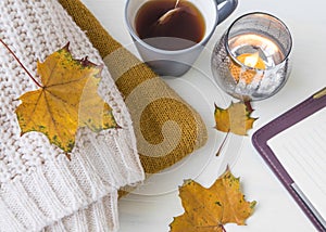 Autumn still life cozy items with woolen sweaters, candle, tea a