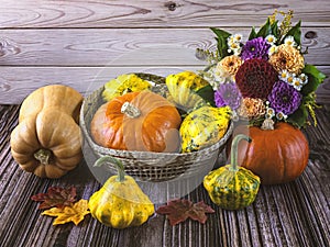 Autumn still life with a harvest of ripe pumpkins in a straw basket, autumn leaves and a bouquet of chrysanthemums