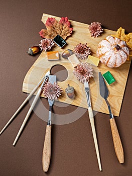Autumn still life with professional art materials, artist`s palette, paints, brushes, acorns, autumn leaves on wooden background.