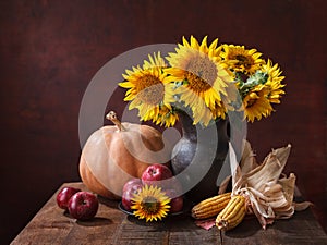 Autumn still life with pumpkin, corns, apples  and bouquet of sunflowers in clay pot on old wooden table