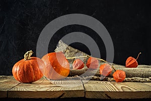 Autumn still life. pumpkins with physalis on a rough burlap and boards on a dark concrete background