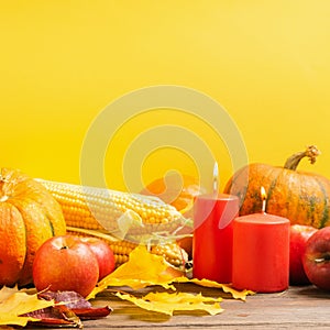 Autumn still life ripe pumpkin apples corn fallen yellow leaves candles yellow background. Thanksgiving Autumn Concept.