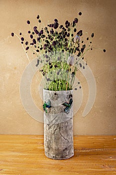 Autumn still life with Sanguisorba officinalis and poppy heads  in handmade ceramic vase with green dragonflies placed on wooden