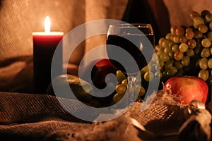 Autumn still life. Thanksgiving post card. Glass full of red wine with candle light reflection and fruits on background