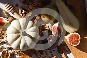 Autumn still-life with white pumpkin, sliced figs, walnuts and pears on wooden cutting board. Healthy eating concept.