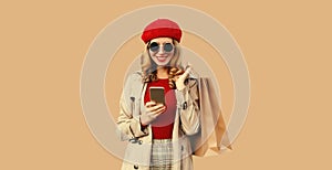 Autumn style outfit, portrait of stylish smiling young woman model with mobile phone holds shopping bags wearing red french beret