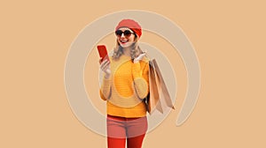 Autumn style outfit, portrait of stylish smiling young woman model with mobile phone holds shopping bags wearing red french beret