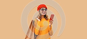 Autumn style outfit, portrait of stylish smiling young woman model with mobile phone holds shopping bags wearing red french beret