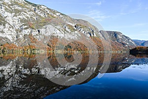 Autumn sunny morning on the Bohinj Lake with the reflection of the mountain