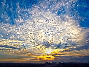 Autumn sunrise with fog. The sun`s rays of the morning sun break through the clouds against the blue sky