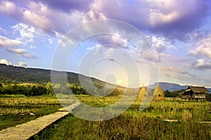 Autumn sunrise in mountainous rural area. Bamboo Walkway and cottage in golden foliage on the meadow in weathered grass. blue sky