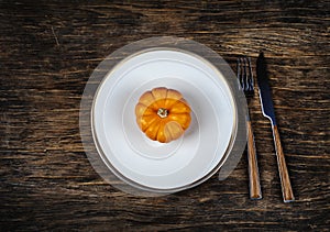 Autumn table setting with plate and pumpkin on wooden background.
